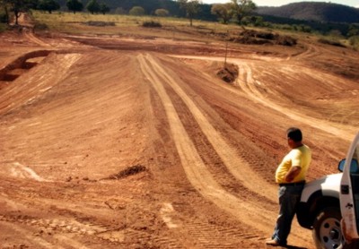 a) Vista superior do macio de terra da barragem – canal extravasor lateral contornando o corpo da barragem.